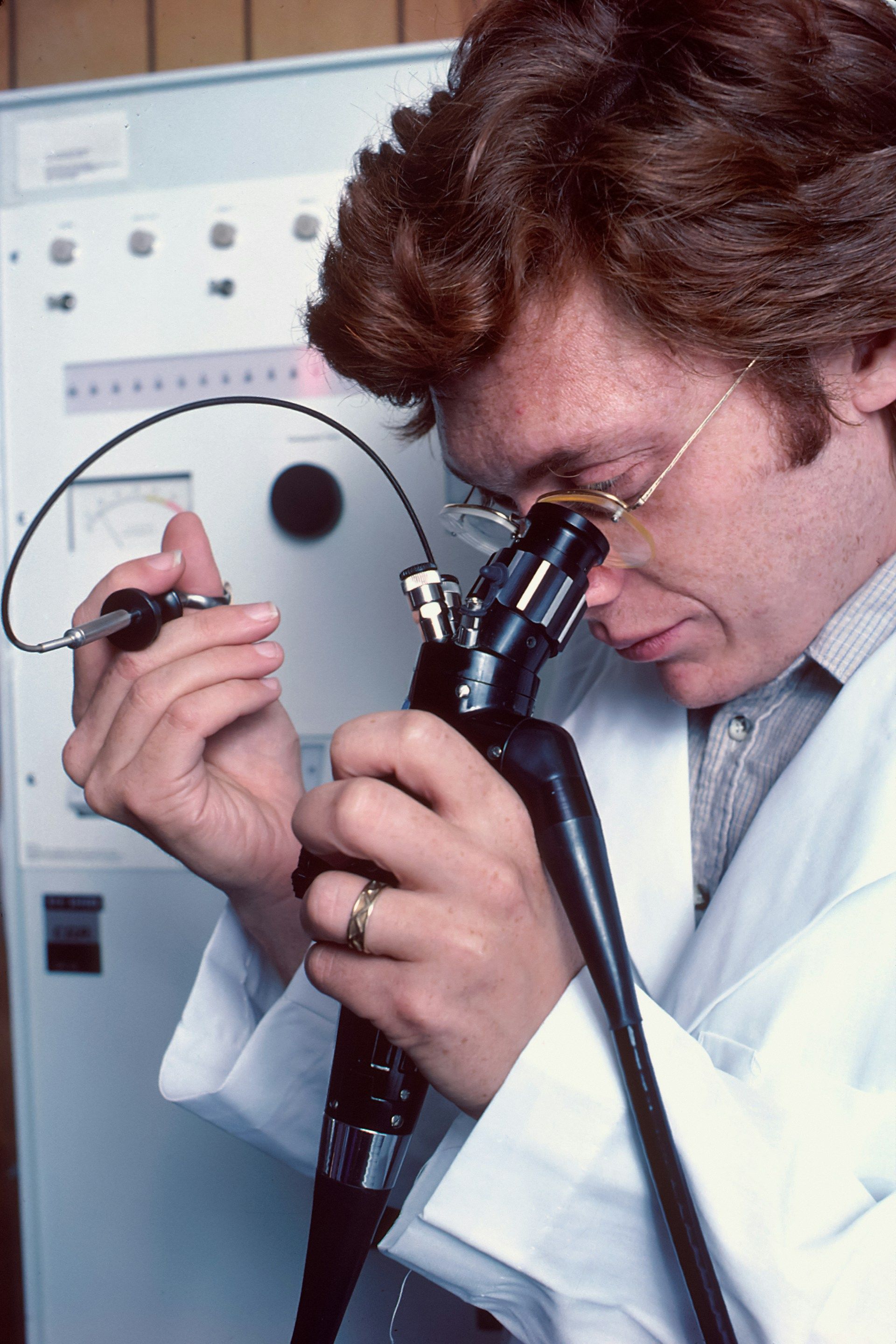 A Caucasian male physician using a remotely controlled endoscope. He is looking through a microscope-like eyepiece to monitor his actions while using small brushes and knives to take a biopsy.